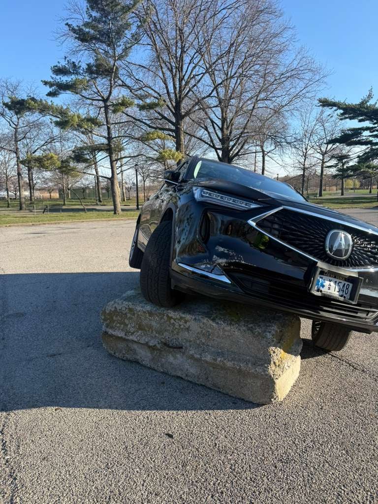 Black Acura MDX lifted off a concrete curb barrier in a Queens park lot — JG Towing recovery.