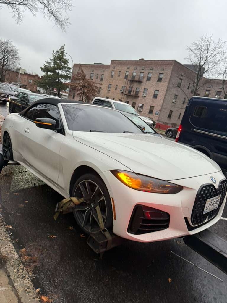 White BMW 4-Series convertible strapped to JG Towing flatbed in Queens on a gray afternoon.