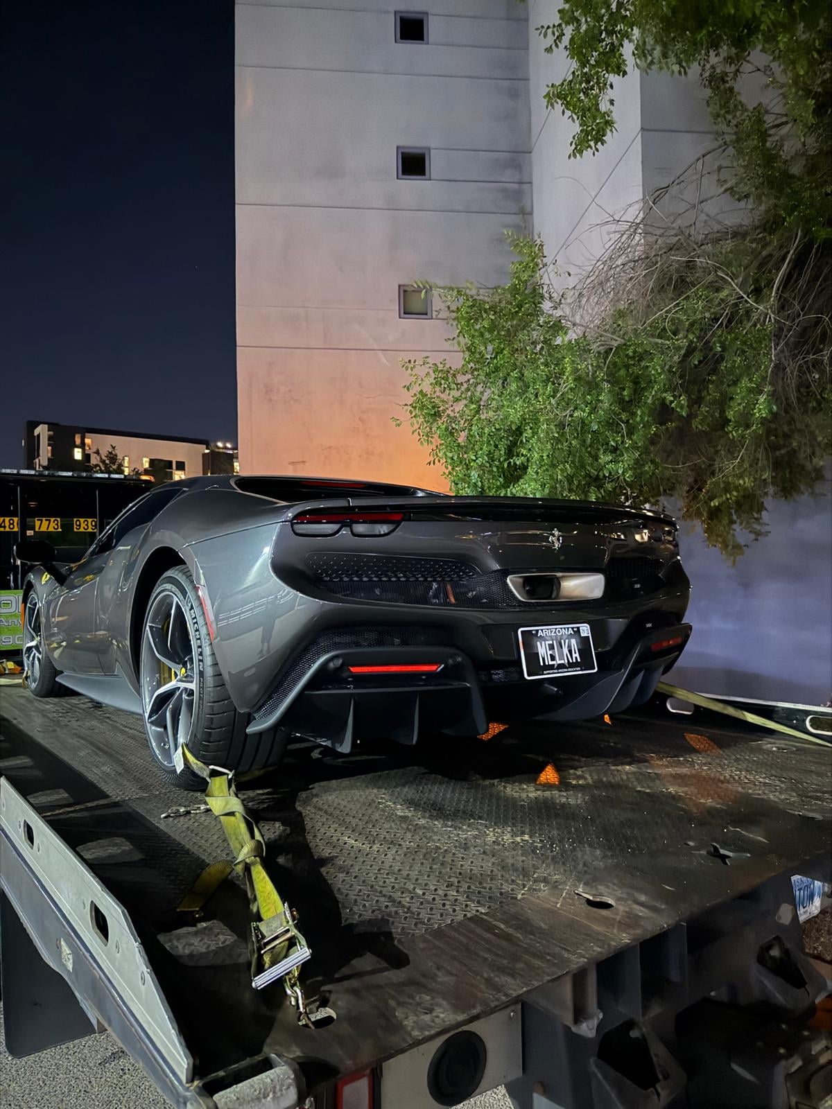 Ferrari 296 GTB secured on JG Towing flatbed at night in front of an apartment tower.