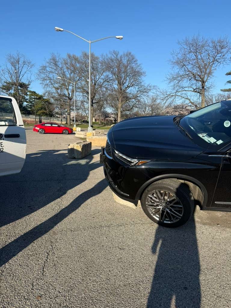 Black Infiniti SUV alongside JG Towing wrecker in a Queens parking lot at golden hour.