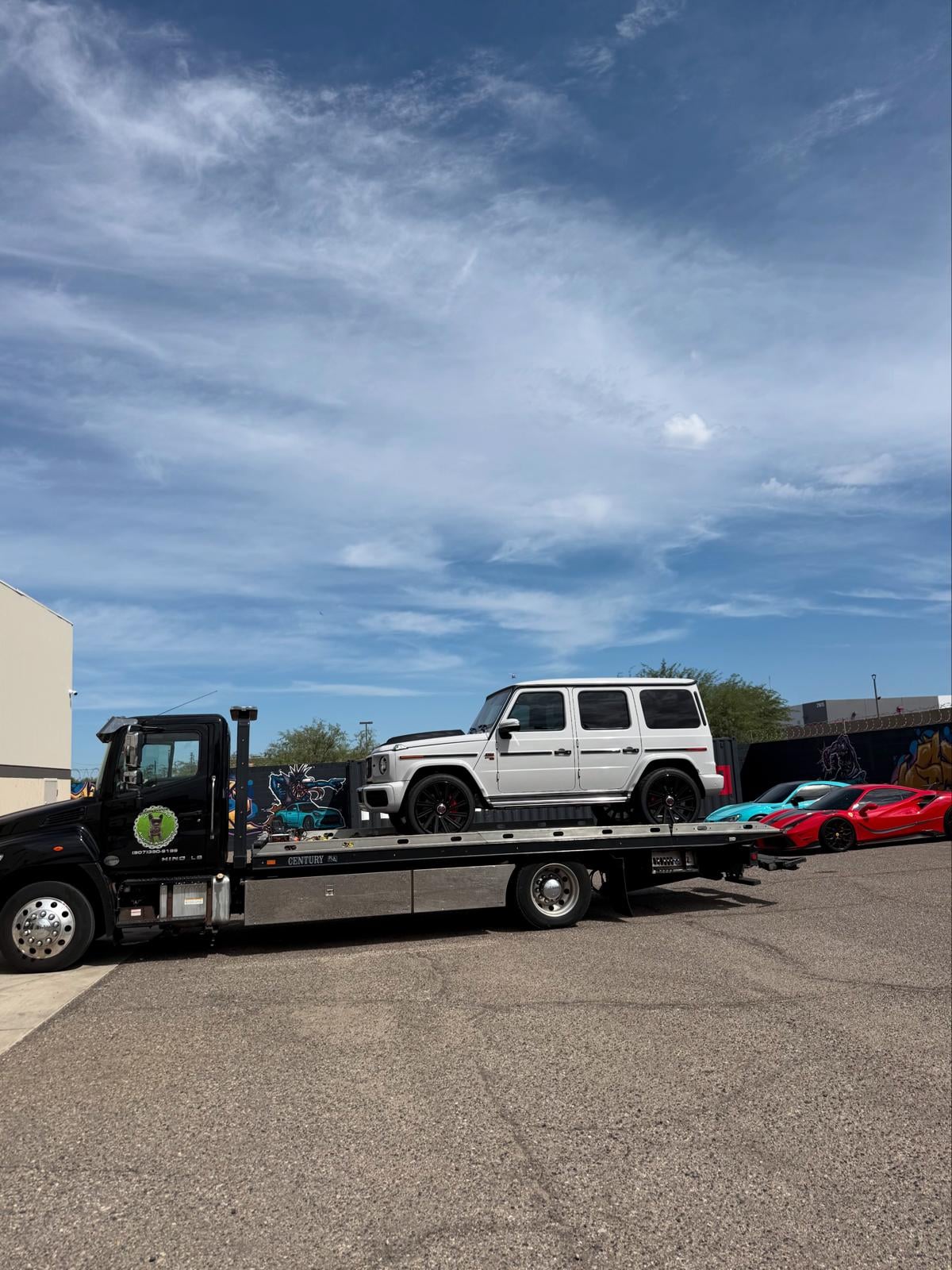 White Mercedes-Benz G-Wagon on JG Towing flatbed beside a Ferrari and exotic hauler.